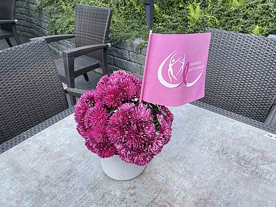 Pinke Blume auf Tisch mit Pink Ribbon Fahne.